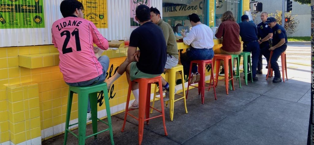 People sitting on colorful stools feast on delicious tacos in Los Feliz on To Live and Dine in LA Food Tours' Los Angeles Taco Tour.