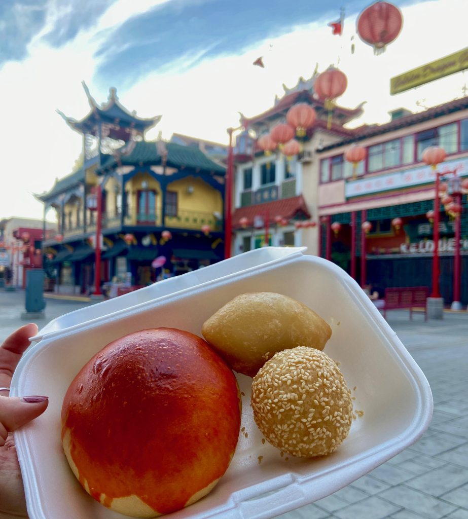 Traditional Chinese pastry - BBQ pork bun, sesame ball, and fried pork bun - with historic Chinatown in downtown Los Angeles in the background on To Live and Dine in LA Food Tours' Chinatown and Olvera Street Food Tour.